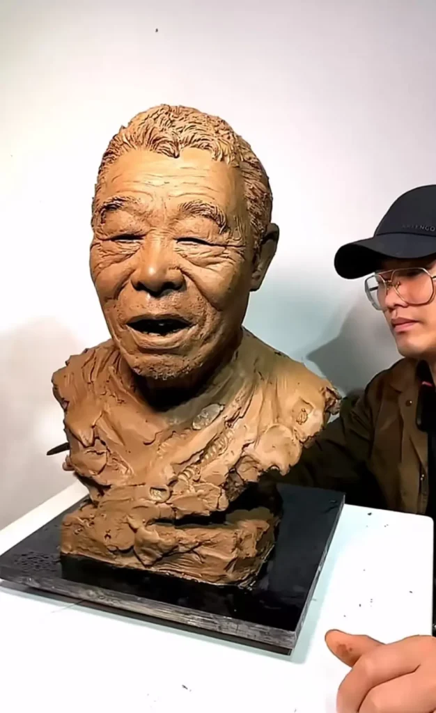 Frontal view of a clay portrait sculpture, highlighting the elder’s calm demeanor and the artist’s ongoing refinement process