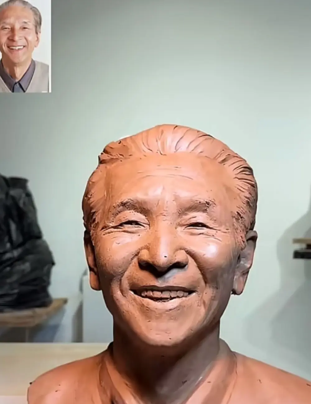 The custom memorial bronze bust for a smiling elderly man in progress, paired with his original photo, highlighting the sculptor’s work to recreate his warm expression.
