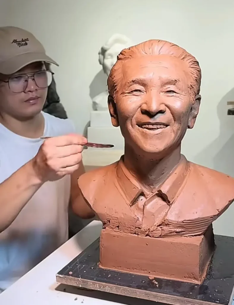 The sculptor refining the custom memorial bronze bust for a smiling elderly man, carefully shaping the details that bring his joyful expression to life.