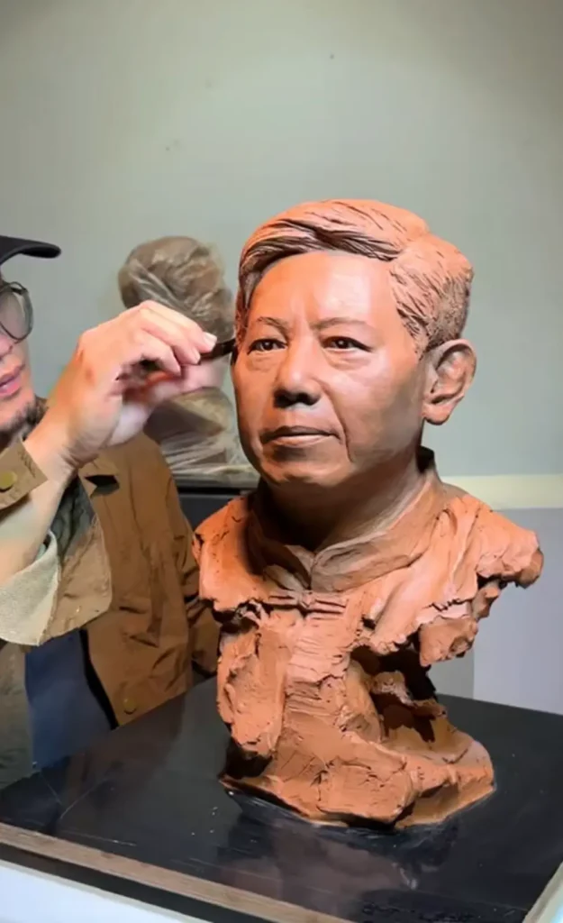 Artist adjusting the clay memorial bust, carefully refining facial details to match the reference photo