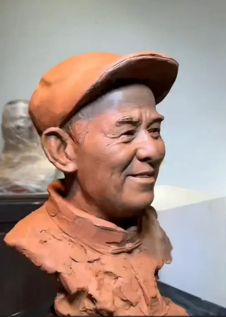 Left profile view of the clay bust, showcasing the sculpted cap texture, ear details, and the natural curve of his smile
