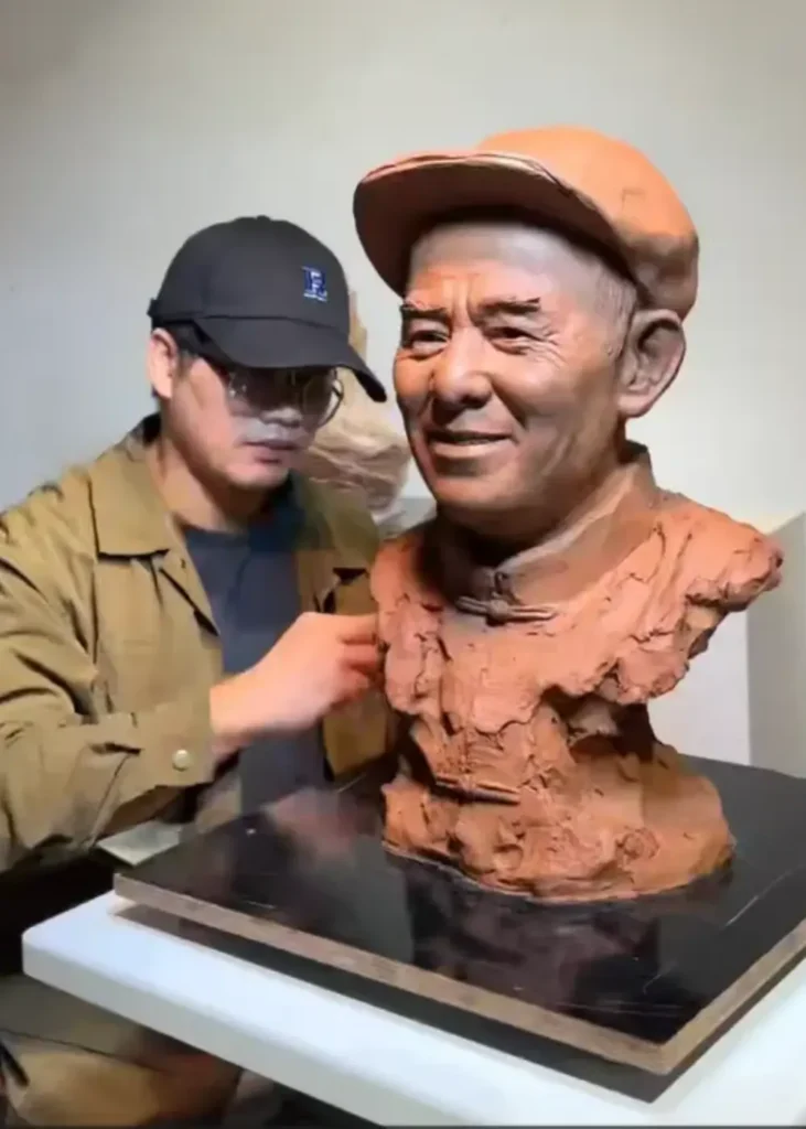 The sculptor adjusting the clay bust in the studio, showing the elderly father’s traditional clothing and cap details