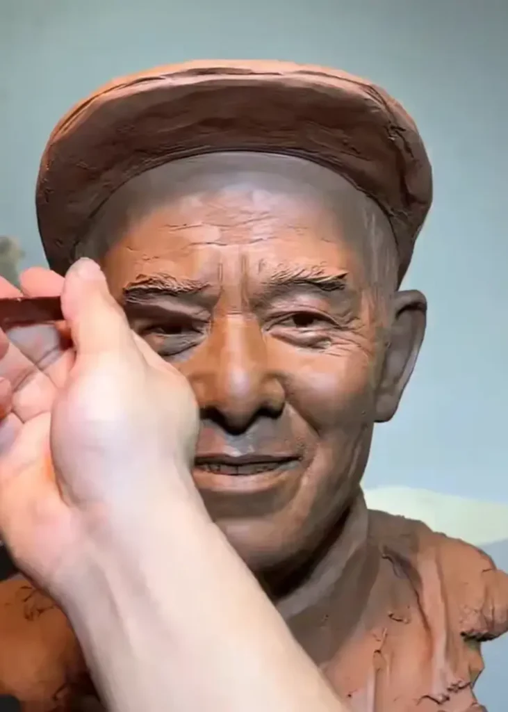 Close-up of the sculptor’s hands refining the clay bust, capturing the elderly father’s gentle smile, facial lines, and hat details