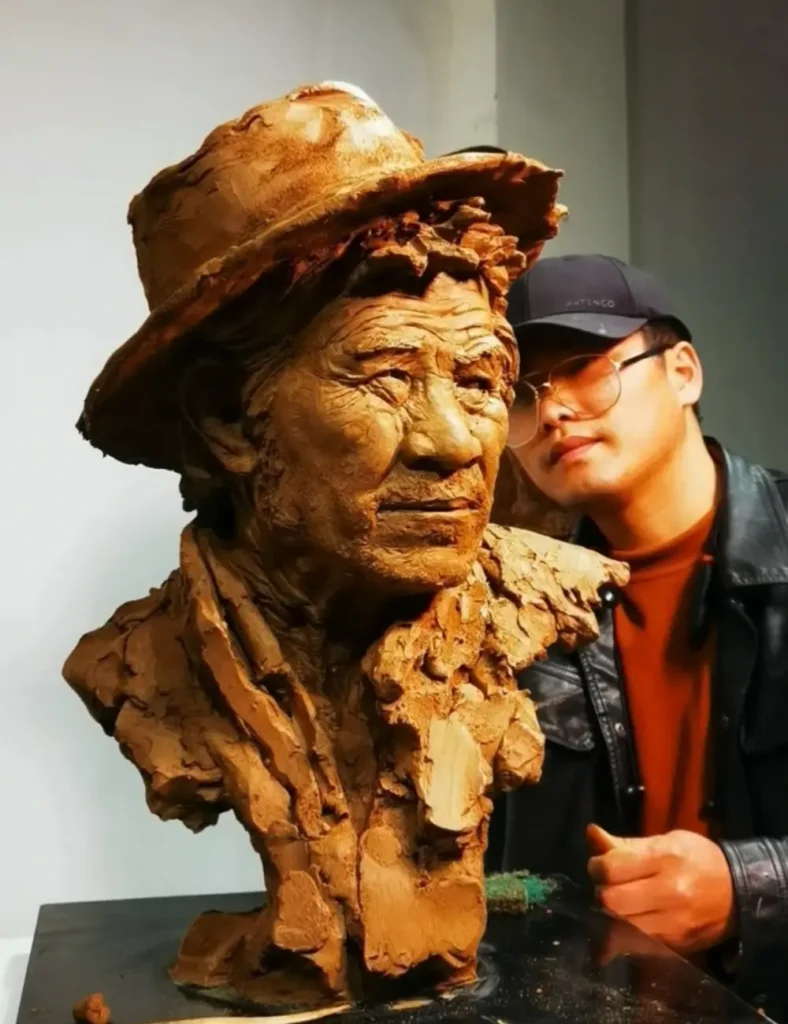 The sculptor standing with the completed clay bust, showing the full form of the elderly man’s portrait, including hat, clothing, and detailed facial features