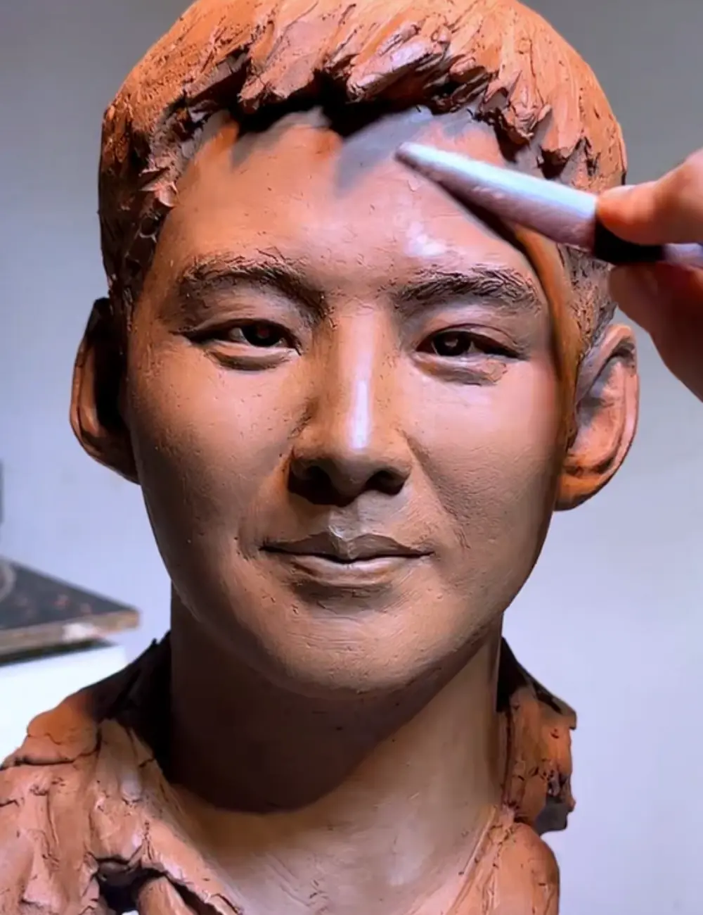 Close-up of the sculptor refining the custom memorial bronze bust for a young adult, focusing on the subtle smile and eye details that capture his personality.