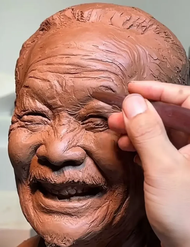The sculptor refining the custom memorial bronze bust for an elderly man, carefully shaping the wrinkles and details that bring his joyful expression to life.